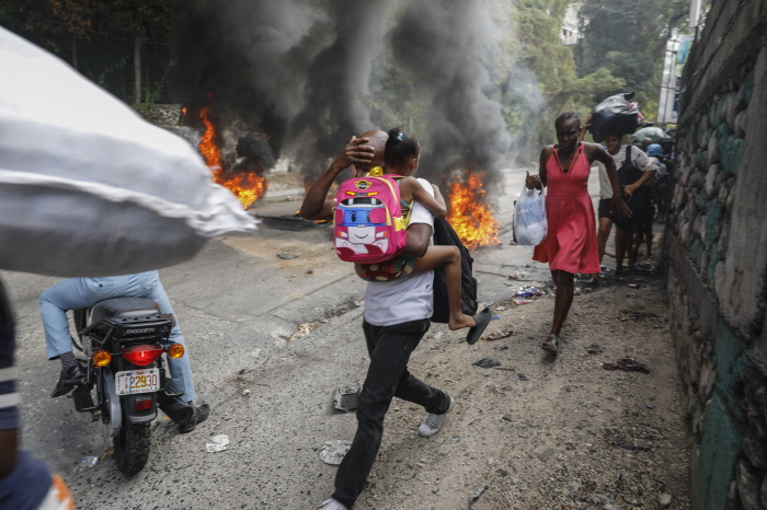 ▲ 지난 2월 5일(현지시각) 아이티 수도 포르토프랭스에서 시위대가 아리엘 앙리 총리의 퇴진을 요구하며 반정부 시위를 하는 동안 주민들이 시위 현장을 황급히 벗어나는 모습. 아이티 전역에서 시위대와 경찰이 충돌하면서 도로가 봉쇄되고 정부 관청 등이 문을 닫는 등 주요 도시 기능이 마비됐다. ⓒAP/뉴시스