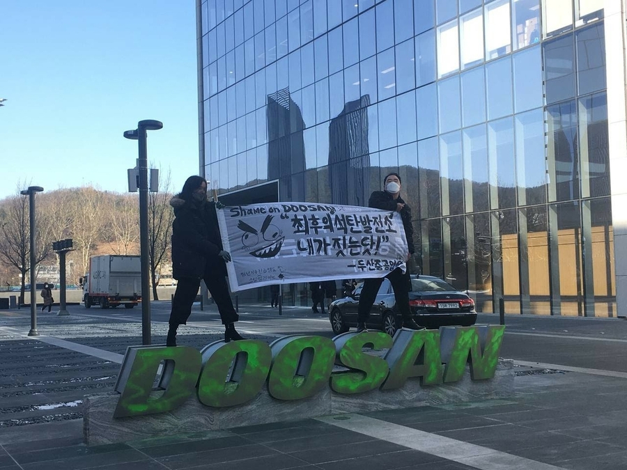 ▲ 청년기후긴급행동 활동가가 2021년 2월18일 경기도 성남시 두산 본사 건물 앞 광장에 설치된 '두산(DOOSAN)' 조형물에 녹색 스프레이를 뿌린 뒤 시위를 하고 있다. ⓒ청년기후긴급행동