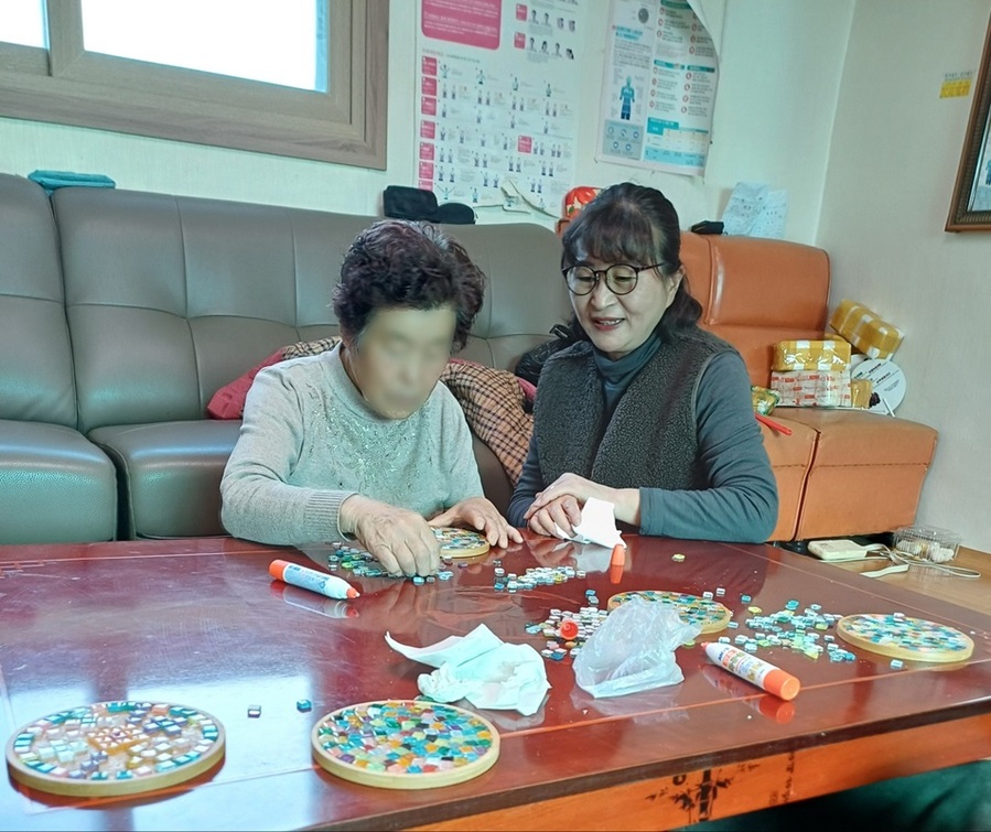 ▲ 괴산군이 식탁위 보석만들기란 주제로 생활지원사가 가가호호 방문해 어르신들과 1대1로 소통하며, 나무 냄비받침 위에 타일 조각을 붙이고 사포질로 완성하는 공예활동을 진행하고 있다.ⓒ괴산군