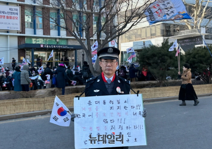 🔼 중국 공안 출신 조선족 난민인 이규호 씨가 윤석열 대통령 탄핵심판 제9차 변론이 진행된 18일 오후 서울 종로구 헌법재판소 인근 안국역 5번 출구에서 시민단체 '엄마부대'(대표 주옥순)가 개최한 탄핵반대 집회 연단에 올랐다. '윤 대통령님의 계엄을 지지한다. 한국에 중국 간첩이 너무 많다. 간첩법을 제정하라'는 피켓을 목에 걸고 중국 공안복 차림으로 나타난 그는