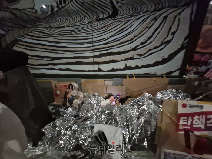 ▲ 23일 자정 서울 종로구 헌재 인근 스타벅스 안국점 앞에서 시민들이 은박 담요를 뒤집어쓰고 릴레이 노숙을 하고 있다. ⓒ조문정 기자