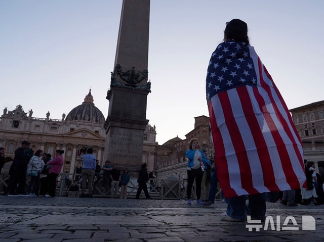 ▲ 미국 출신의 레오 14세 교황이 선출된 뒤 성베드로 대성전 '강복의 발코니'에 모습을 드러내자 한 신자가 성조기를 두르고 기뻐하고 있다. 250508 AP/뉴시스. ⓒ뉴시스