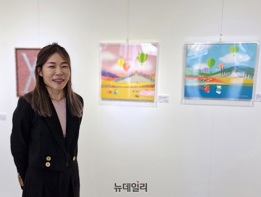 ▲ 청주대학교 정문 앞 ‘갤러리 젠(ZEN)’에서 열리고있는 전시회에서 마가렛윤정 작가가 작품 앞에서 밝게 웃고 있다.ⓒ양승갑 기자