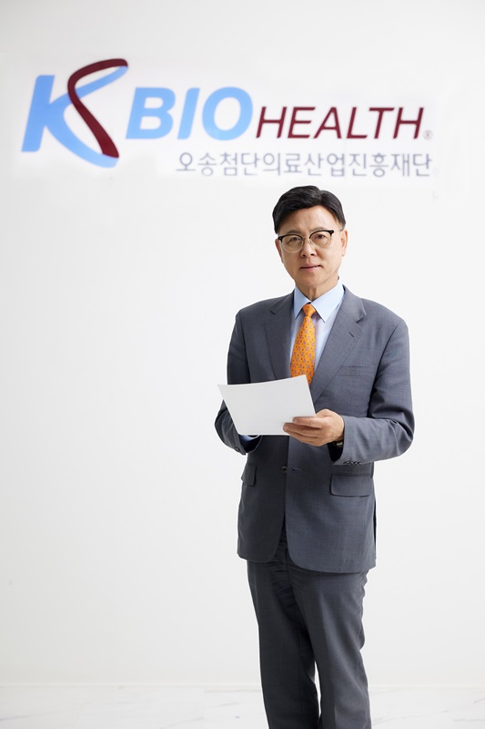 ▲ 이명수 KBIOHealth 이사장이 사무실에서 KBIOHealth 로그를 배경으로 기념촬영을 하고 있다.ⓒKBIOHealth