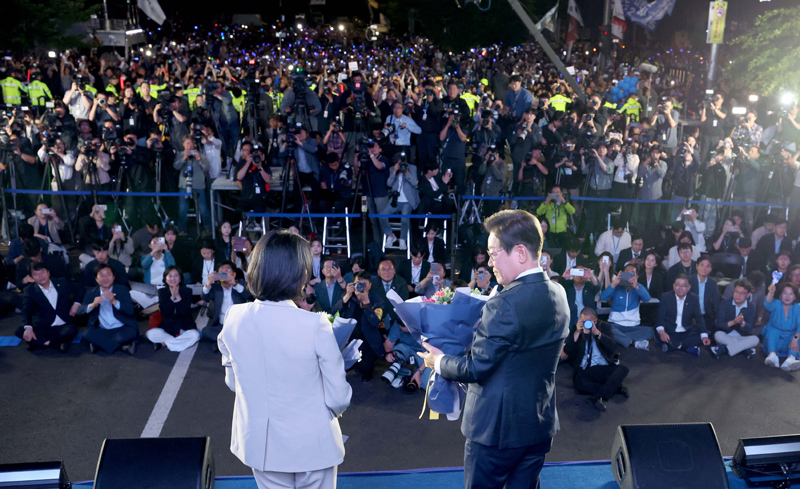 ▲ 이재명 대통령과 김혜경 여사가 4일 오전 서울 여의도 국회 앞에서 열린 국민 개표방송 행사에서 꽃다발을 받은 뒤 마주보고 있다. ⓒ뉴시스
