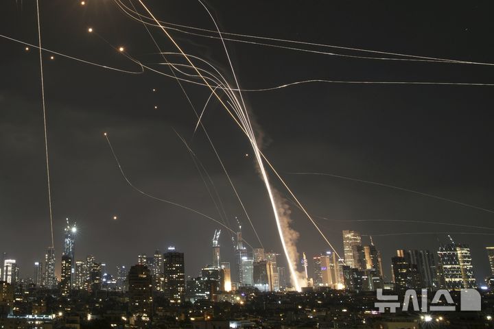 ▲ 13일(현지 시간) 이스라엘 텔아비브 상공에서 아이언돔 방공 시스템이 미사일을 요격하는 가운데, 발사체가 건물을 강타하고 있다. ⓒ뉴시스(사진=AP)