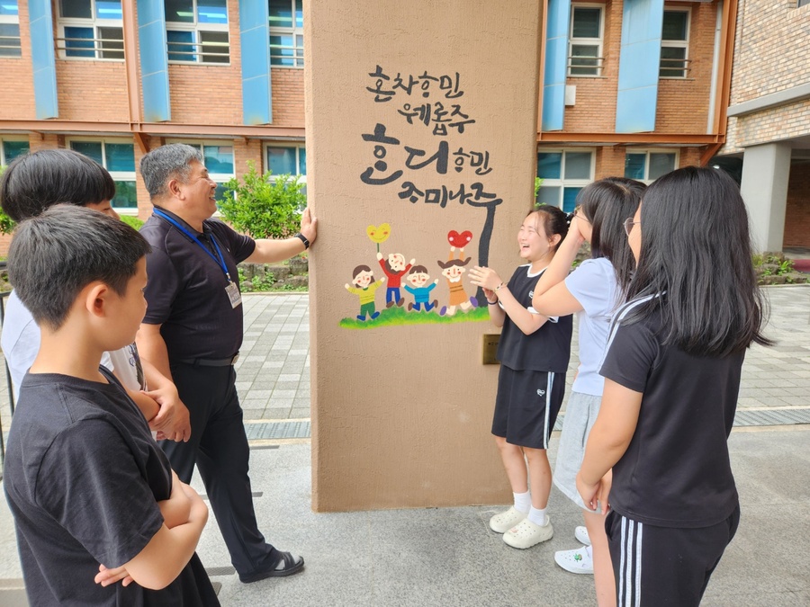 ▲ 19일 강동헌 신제주초등학교 교장이 교정 외벽에 아로새겨진 제주어 벽화의 글귀 의미에 관해 학생들에게 설명하고 있다. ⓒ신제주초등학교 제공