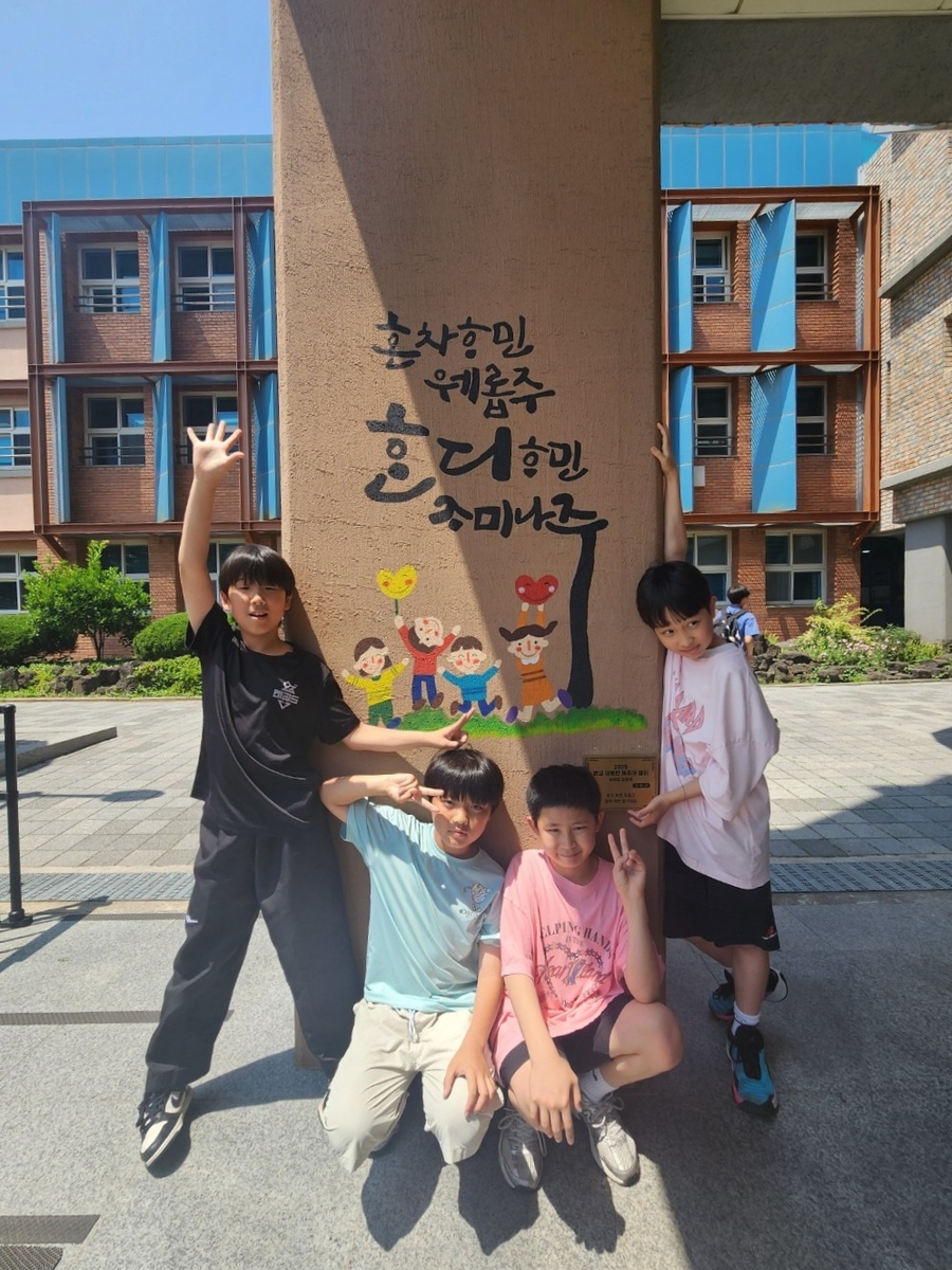▲ 신제주초등학교 학생들이 학교 외벽에 아로새겨진 제주어 벽화 앞에서 사진을 찍고 있다. ⓒ제주특별자치도교육청 제공