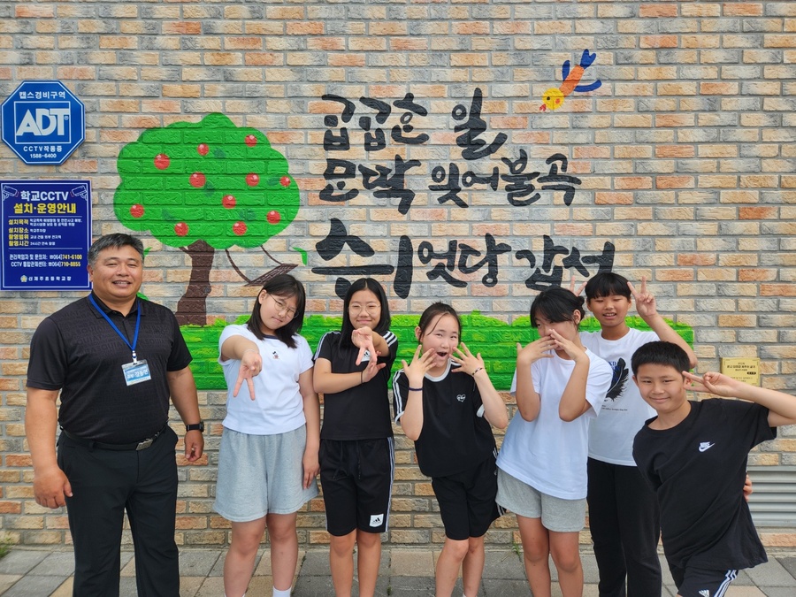 ▲ 19일 강동헌 신제주초등학교 교장이 학생들에게 교정 외벽에 아로새겨진 제주어 벽화의 글귀 의미에 관해 학생들에게 설명한 후 사진 촬영을 하고 있다. ⓒ신제주초등학교 제공