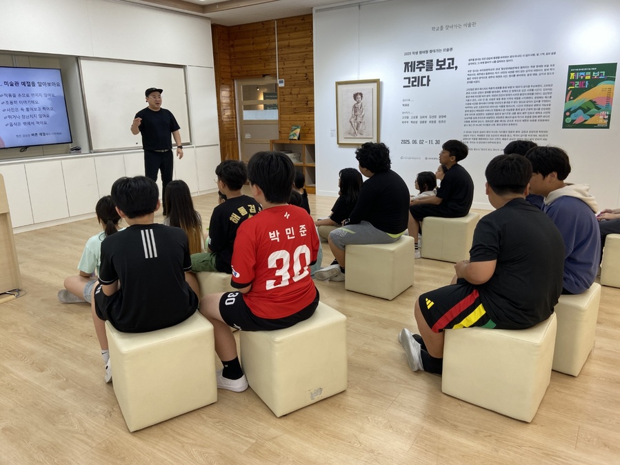 ▲ 하귀초등학교 학생들이‘학생 참여형 찾아가는 미술관–제주를 보고 그리다’전시회에 전시된 작품에 관한 작품 해설을 듣고 있다. ⓒ제주특별자치도교육청 제공