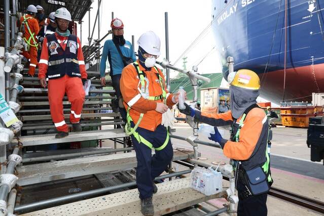 ▲ 한화오션 안전관리자가 '찾아가는 얼음생수' 활동으로 오후 쉬는 시간 휴식을 위해 하선하는 작업자들에게 얼음 생수를 전달하고 있다. ⓒ한화오션