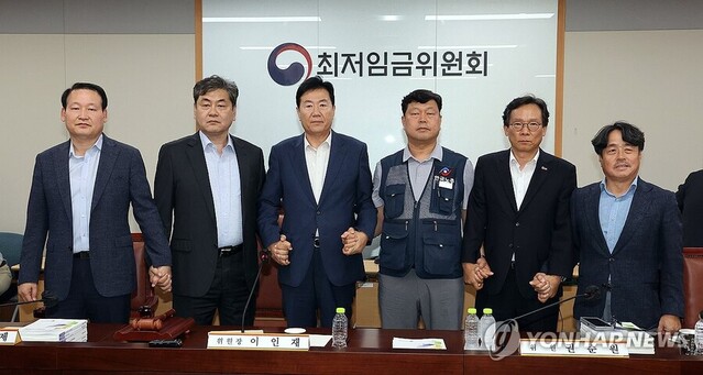 ▲ 10일 정부세종청사에서 열린 제12차 전원회의에서 내년 최저임금을 시간당 1만320원으로 17년만에 합의로 결정한 공익위원-사용자위원-근로자위원들이 손을 잡고 기념촬영을 하고 있다. ⓒ연합뉴스