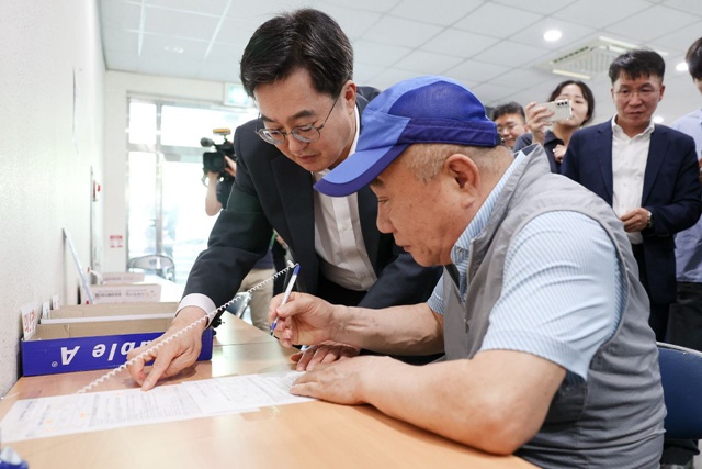 ▲ 김동연 경기도지사가 지난 21일 수원시 원천동 행정복지센터에서 '민생회복 소비쿠폰'을 현장 접수 중인 시민을 돕고 있다. ⓒ경기도 제공