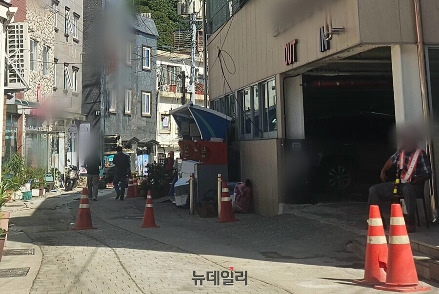 ▲ 관공서 및 상가, 공영주자창 등이 밀집돼 있는 공사 현장서 수신호를 보는 한 작업자가 무더위 속 식곤증(음식을 먹은 후 졸음이 오는 현상)을 이기지 못한 듯 한 켠에 앉아 있다.ⓒ뉴데일리