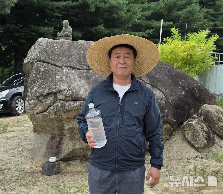 ▲ 왕두꺼비 산장 신승우 대표가 식당 마당에 있는 두꺼비 바위 앞에서 천연 아연이 함유된 금율약수를 들고 촬영을 하고있다.ⓒ