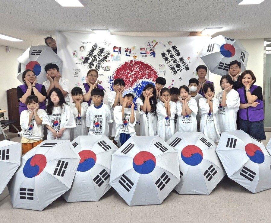 ▲ 광복 80주년을 기념한 ‘대형 태극기 만들기’ 행사에 참여한 청소년들이 태극기 문양이 새겨진 티셔츠를 입고, 직접 만든 대형 태극기 앞에서 기념촬영을 하고 있다.ⓒ수성구