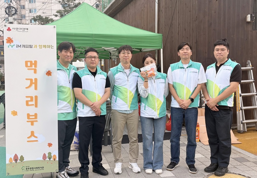 ▲ iM캐피탈 직원들이 ‘경로의 달’ 행사 먹거리 부스 앞에서 후원 기념사진을 촬영을 하고 있다.ⓒiM캐피탈