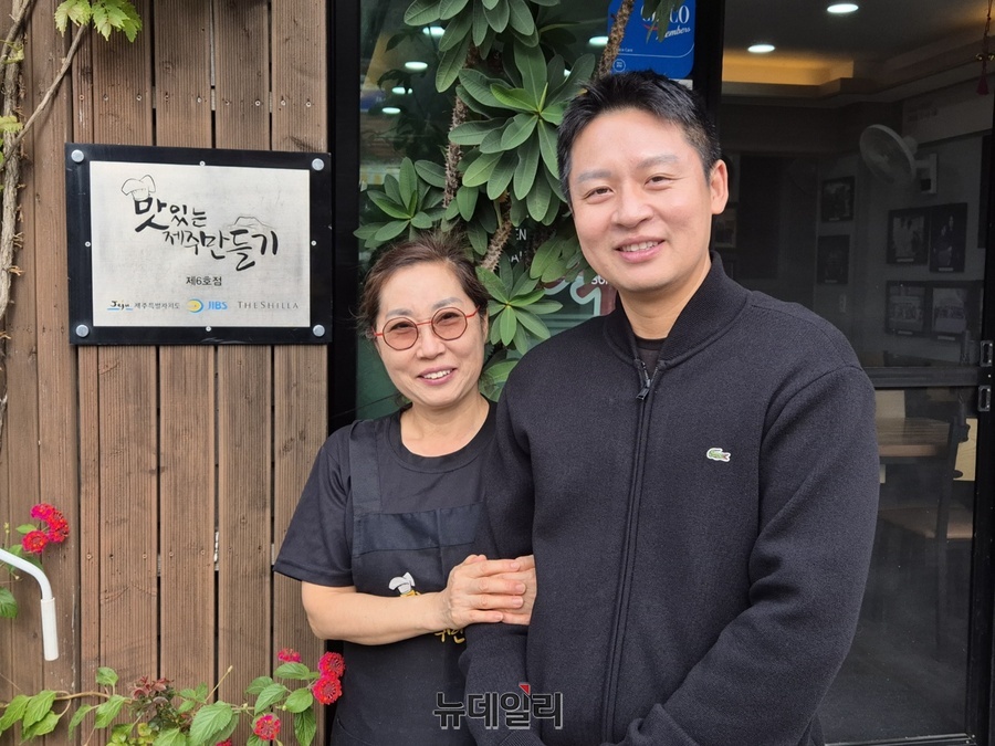 ▲ 홍수정 진미네식당 사장과 박영준 호텔신라 셰프가 '맛제주' 현판 옆에서 기념촬영을 하고 있다.ⓒ조현우 기자