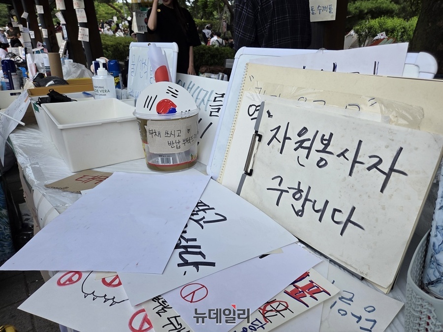 14일 오후 서울 송파구 올림픽공원 핸드볼 경기장 인근 시위 현장 입구에 설치된 부스 위로 '자원봉사자를 구한다'는 안내문이 놓여 있다. Ⓒ노유지 기자