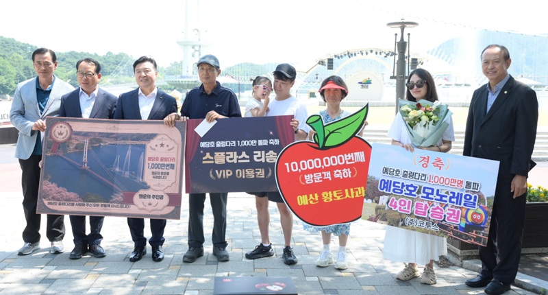 ▲ 예산군 예당호 출렁다리 누적 방문객 1000만 명 달성을 기념해 최재구 예산군수(왼쪽 세 번째)와 관계자들이 1000만 번째 방문객으로 선정된 당진시 합덕읍 김건호 씨 가족에게 기념품과 꽃다발을 전달한 뒤 기념촬영을 하고 있다.ⓒ예산군